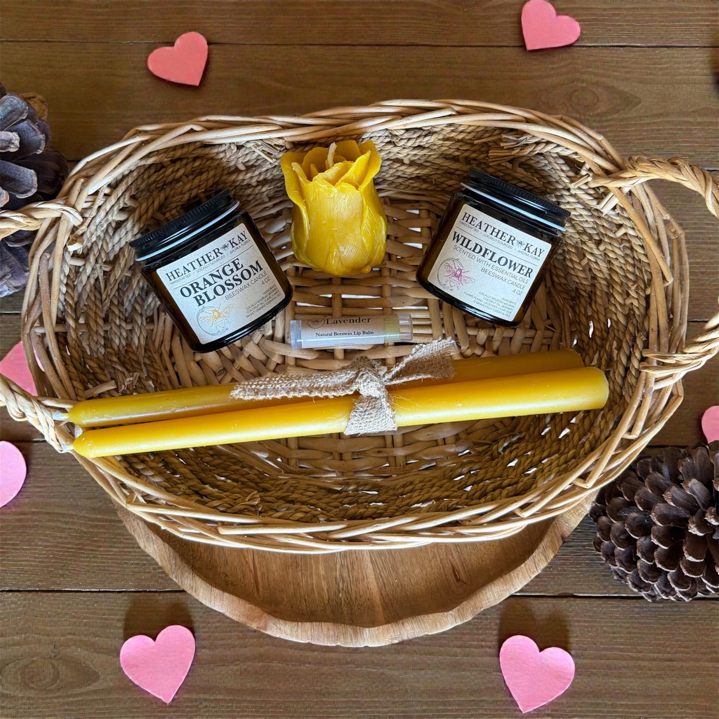 Wicker basket with candles and a yellow candle on a wooden surface with heart decorations.